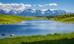 a grassy meadow is near a lake with snow capped mountains in the distance