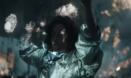 a man in a green raincoat holds his arms up