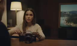 a woman holding onto a camera and sitting in front of a man