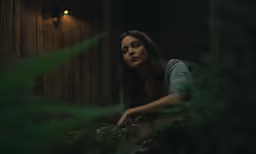 a young girl sitting on the ground by a wood wall in a forest