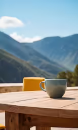 a table with a cup and two chairs and mountains in the background