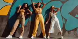 three women standing in front of a wall and wearing different colored jumpsuits