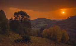the sun setting behind trees in the hills